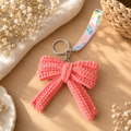 Pink handmade crochet bow keychain with colorful wrist strap on wooden surface