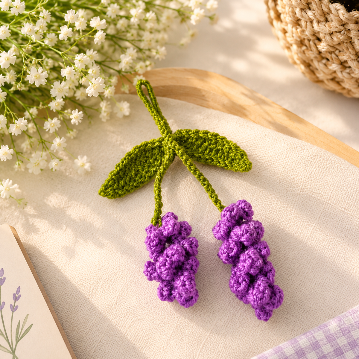 Handmade purple grape crochet keychain with green leaves on a beige fabric background